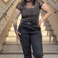 A person wearing a black mesh top with short sleeves and a mock turtle neck, featuring soft velvet bows, paired with black pants.