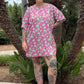 Person wearing a pink dress with green patterns standing outdoors with palm trees in the background