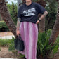 Person wearing a black t-shirt and pink pants standing in front of palm trees.