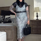 A person wearing a sleeveless, spaghetti strap, midi-length dress with a leopard print design, paired with a black belt, shoes, and carrying a black bag.