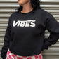 Person wearing a black sweatshirt with 'VIBES' text, standing against a metallic shutter.
