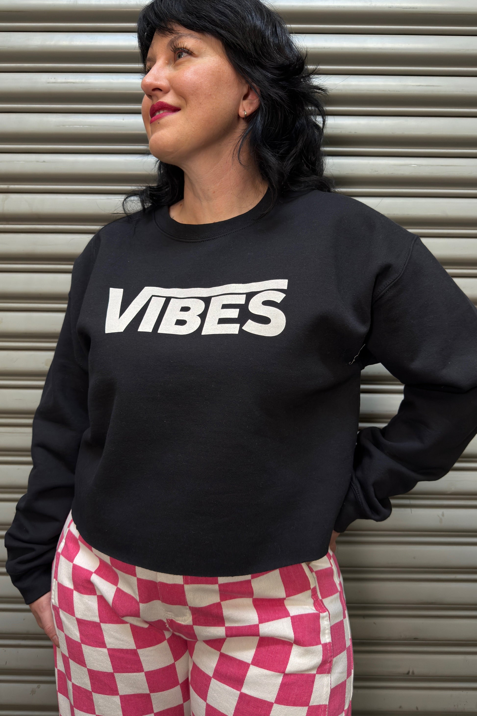 Person wearing a black sweatshirt with 'VIBES' text, standing against a metallic shutter.