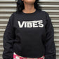 Person wearing a black sweatshirt with 'VIBES' text in front of a metallic shutter.
