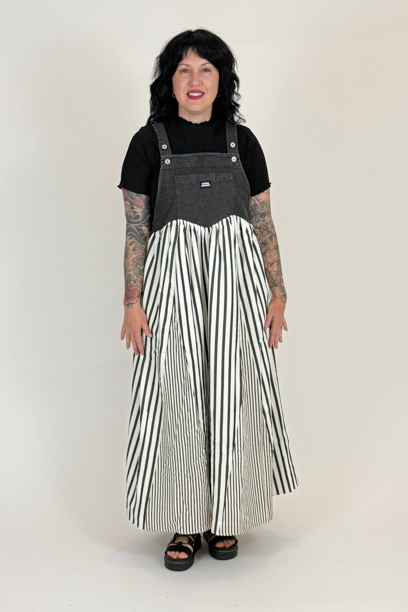 Person wearing a black t-shirt and striped overalls on a white background