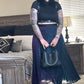 Person wearing a black top and purple pleated skirt in a living room.