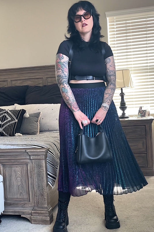 Person wearing a black top and purple pleated skirt in a living room.