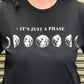 Black t-shirt with moon phase design and 'It's Just a Phase' text worn by a person.