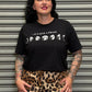 Person wearing a black t-shirt with white text and graphics, standing in front of a metallic shutter.