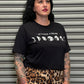 Person wearing a black t-shirt with text and moon phases graphic, standing in front of a metallic shutter.