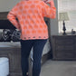 Person wearing a pink sweater with orange patterns in a bedroom setting.