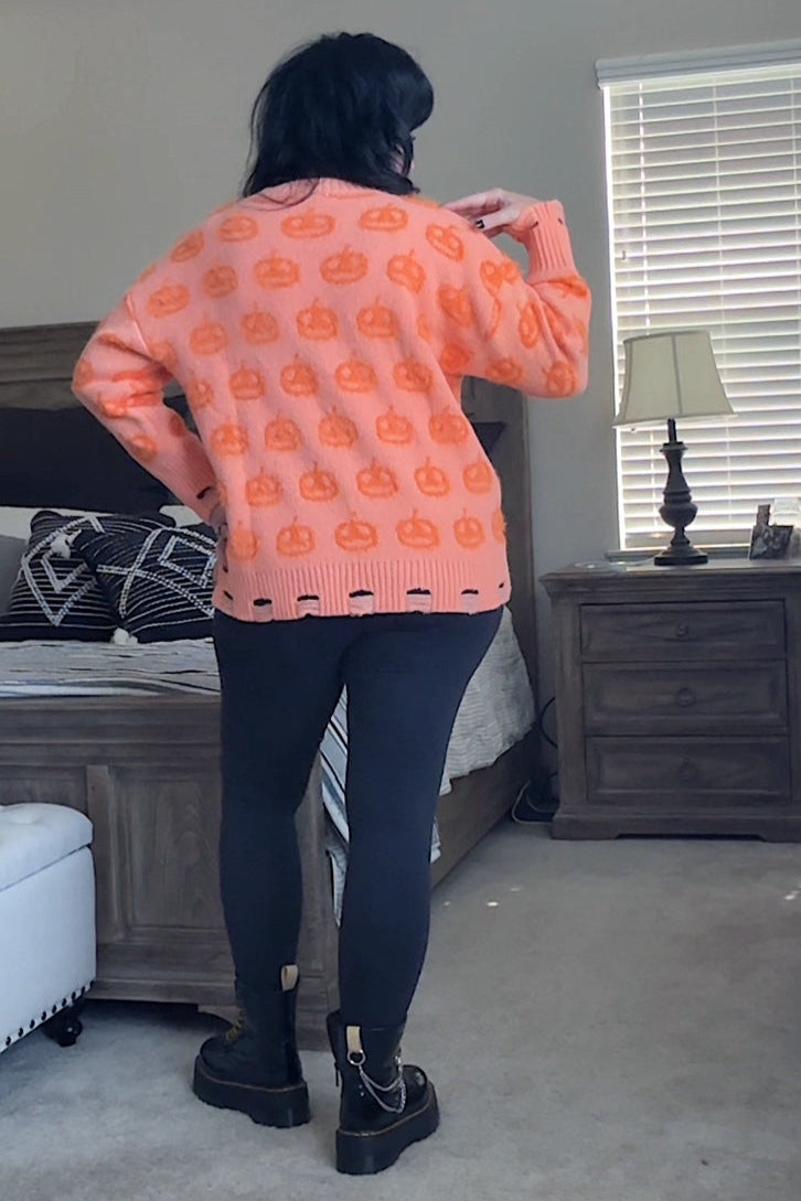 Person wearing a pink sweater with orange patterns in a bedroom setting.