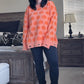 Person wearing an orange sweater with orange pumpkin patterns in a bedroom setting.