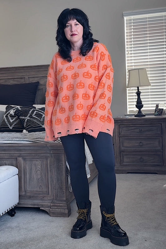 Person wearing an orange sweater with orange pumpkin patterns in a bedroom setting.