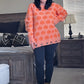 Person wearing an orange sweater with black pumpkin pattern in a bedroom setting