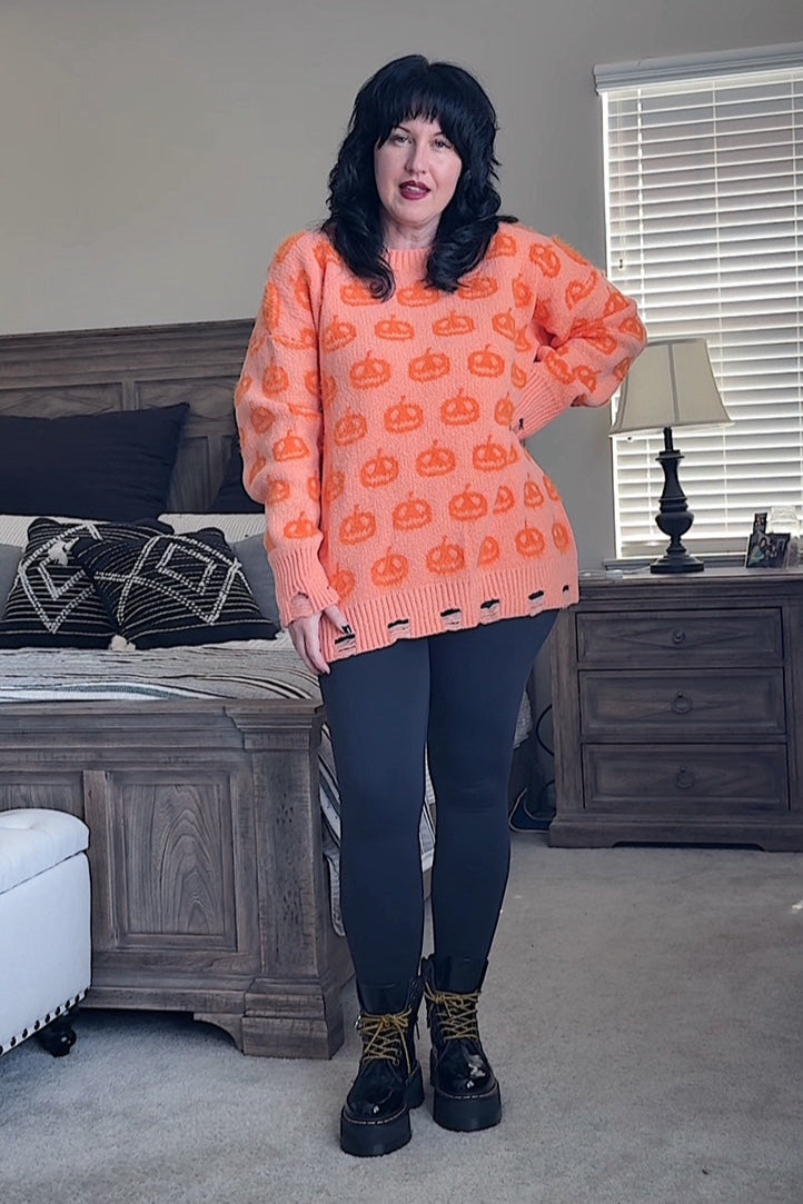 Person wearing an orange sweater with black pumpkin pattern in a bedroom setting