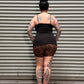 A person viewed from above, wearing a black sleeveless top and leopard-print shorts, standing against a gray corrugated metal wall.