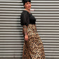 A person wearing leopard-print pants and a black top stands in front of a gray corrugated metal shutter.