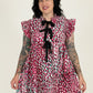 Woman wearing a colorful patterned dress with ruffled sleeves against a plain background