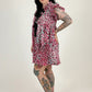 Person wearing a patterned dress with tattoos standing against a white background