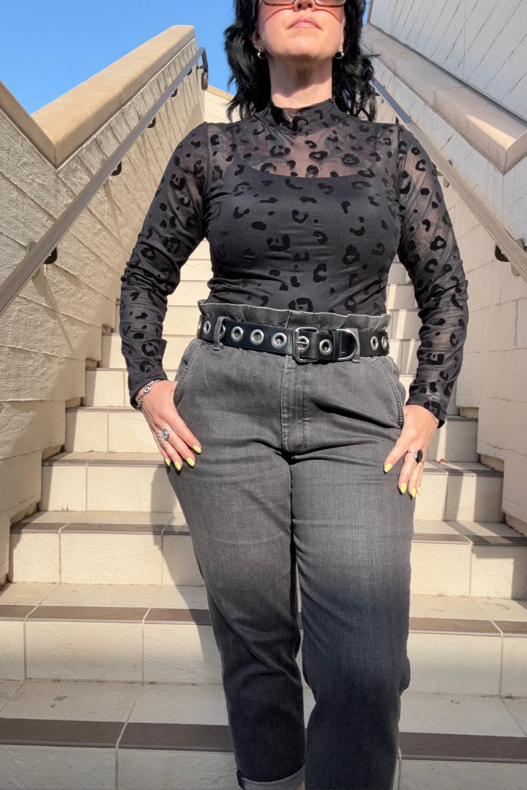 Person wearing a patterned shirt and gray jeans standing on steps with a blue sky background