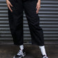 Person wearing a checkered shirt, black pants, and black sneakers against a metallic shutter background