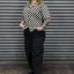Person wearing a black and white checkered shirt and black pants standing in front of a metal shutter.