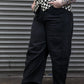 Person wearing a black and white checkered shirt, black pants, and black shoes against a metallic shutter background.