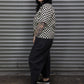 Person wearing a black and white checkered shirt with black pants standing in front of a metallic shutter.