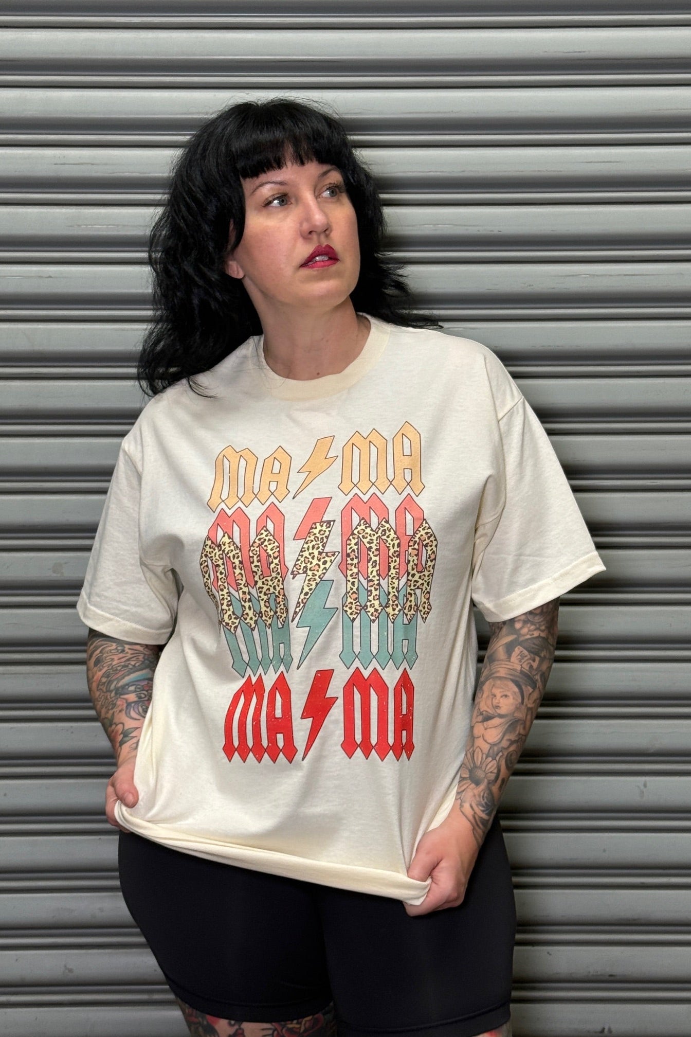 Person wearing a white t-shirt with colorful text design against a metallic shutter background