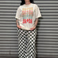 Person wearing a graphic t-shirt and checkered pants standing in front of a metal shutter.