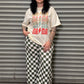 Person wearing a graphic t-shirt and checkered pants standing in front of a metal shutter.