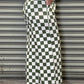Person wearing green and white checkered pants leaning against a metallic shutter.