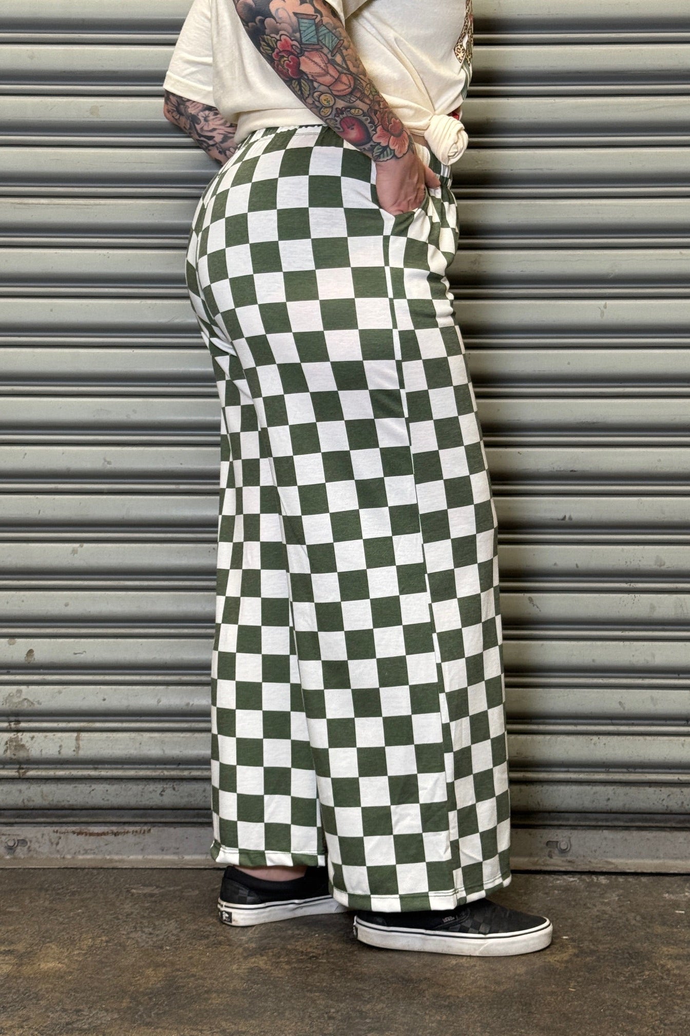 Person wearing green and white checkered pants leaning against a metallic shutter.