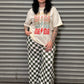 Person wearing a graphic t-shirt and checkered pants standing in front of a metal shutter.