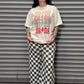 Person wearing a graphic t-shirt and checkered pants standing in front of a metal shutter.