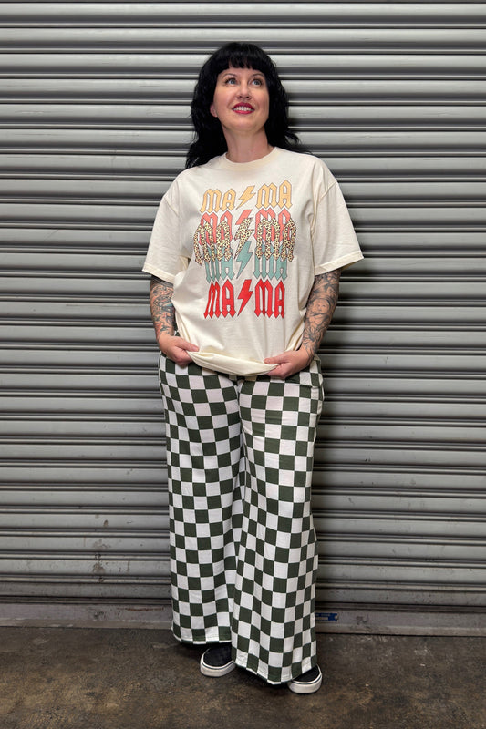 Person wearing a graphic t-shirt and checkered pants standing in front of a metal shutter.