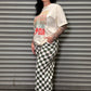 Person wearing a graphic t-shirt and checkered pants leaning against a metal shutter.