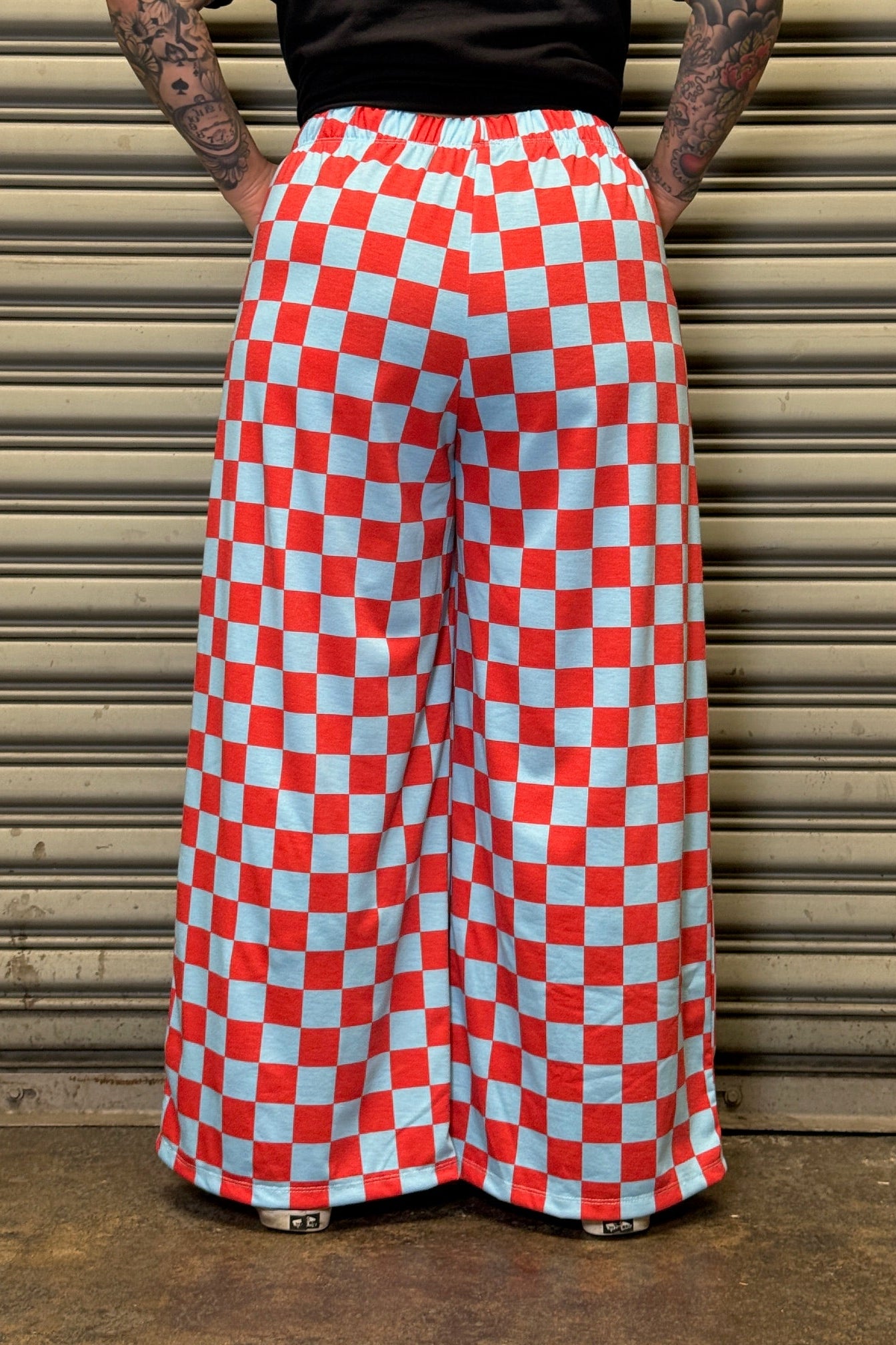 Person wearing red and white checkered pants standing against a metallic shutter.
