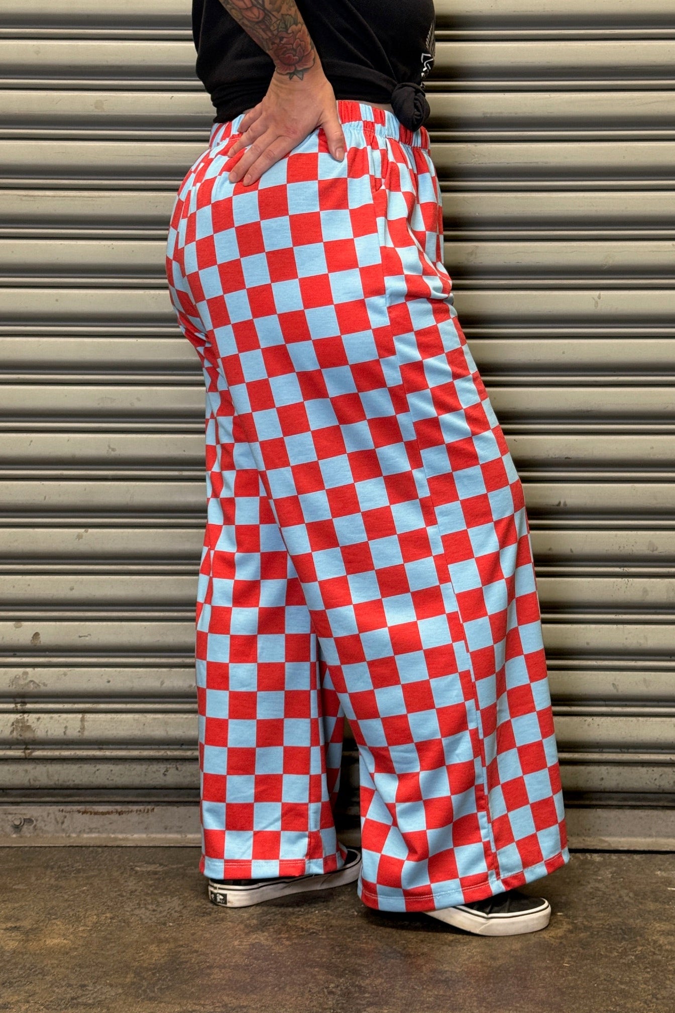Person wearing red and white checkered pants standing against a metallic shutter.