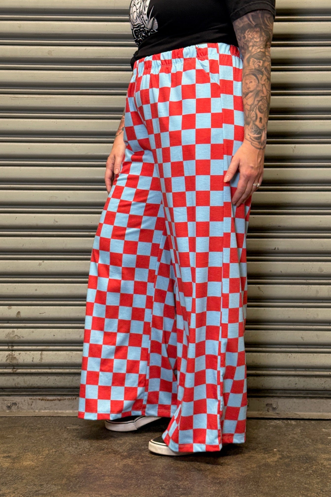 Person wearing red and white checkered pants standing against a metal shutter.