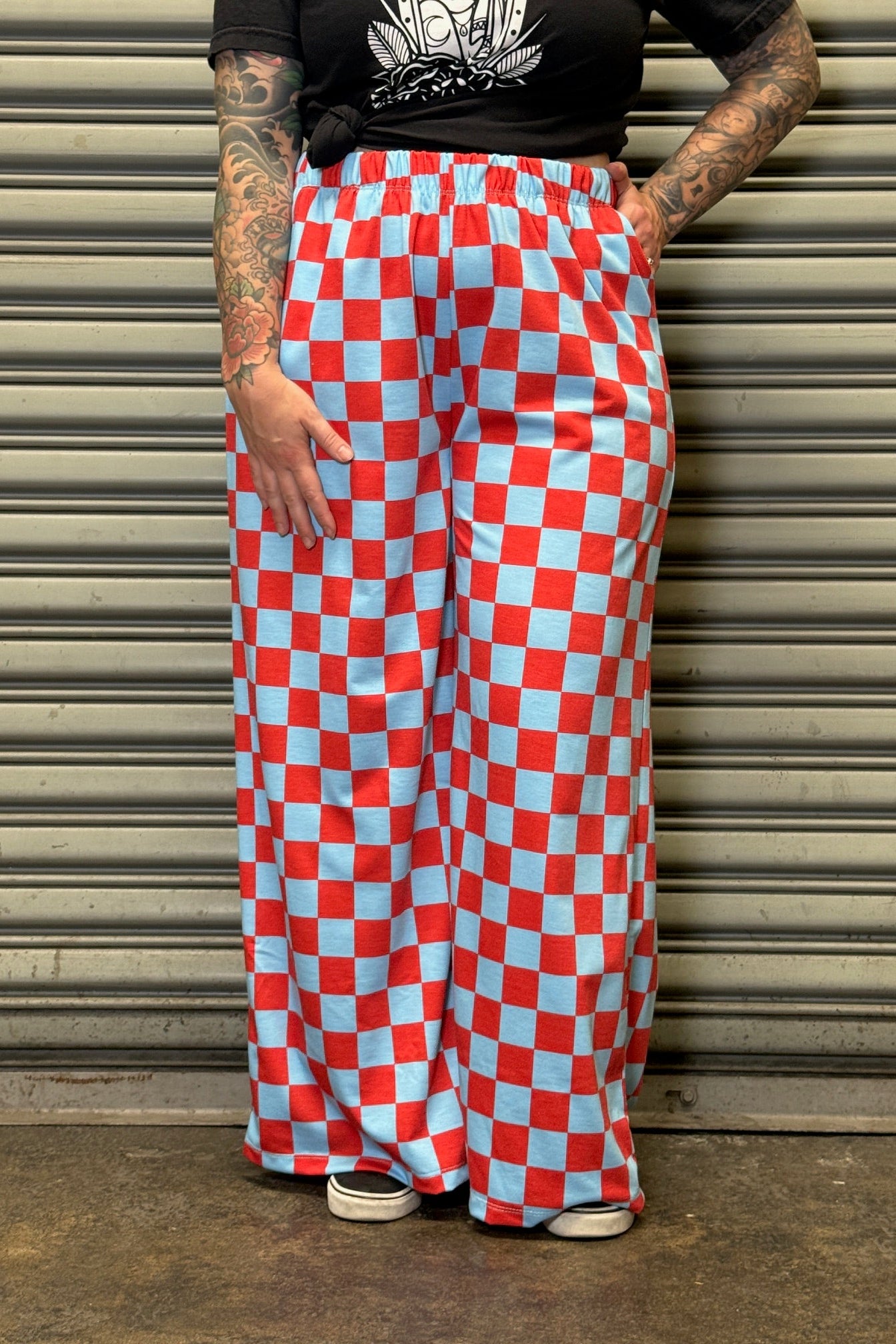 Person wearing red and blue checkered pants standing against a metallic shutter.