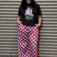 Woman wearing a black t-shirt with a graphic design and red and blue checkered pants standing against a metal shutter.