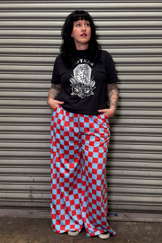 Woman wearing a black t-shirt with a graphic design and red and blue checkered pants standing against a metal shutter.