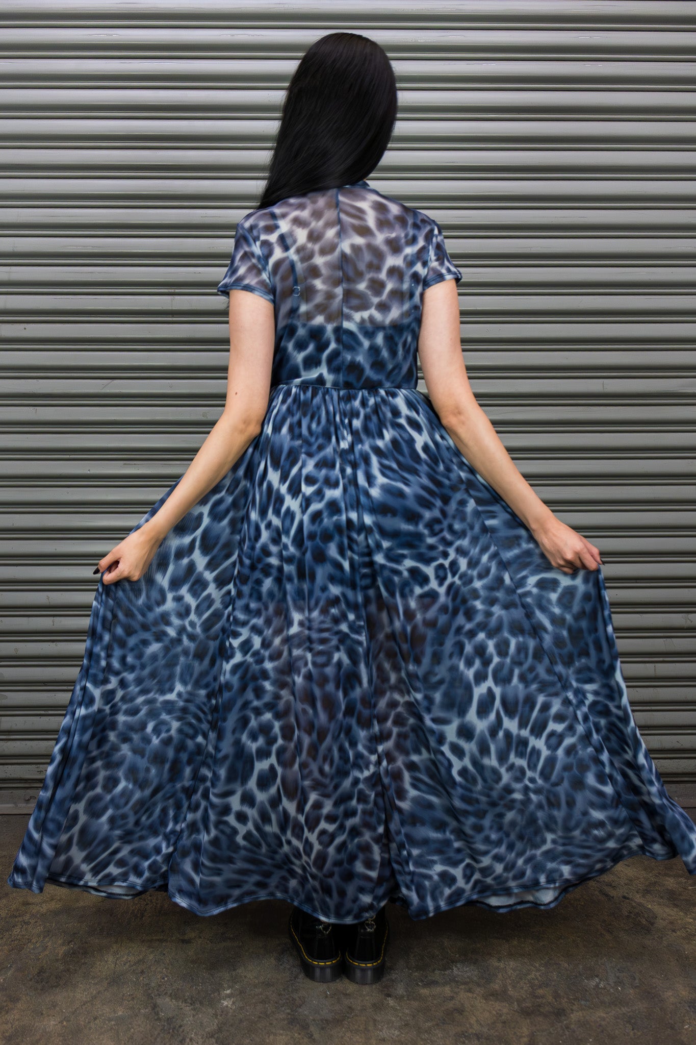 Woman wearing a blue leopard print dress standing in front of a metallic shutter.