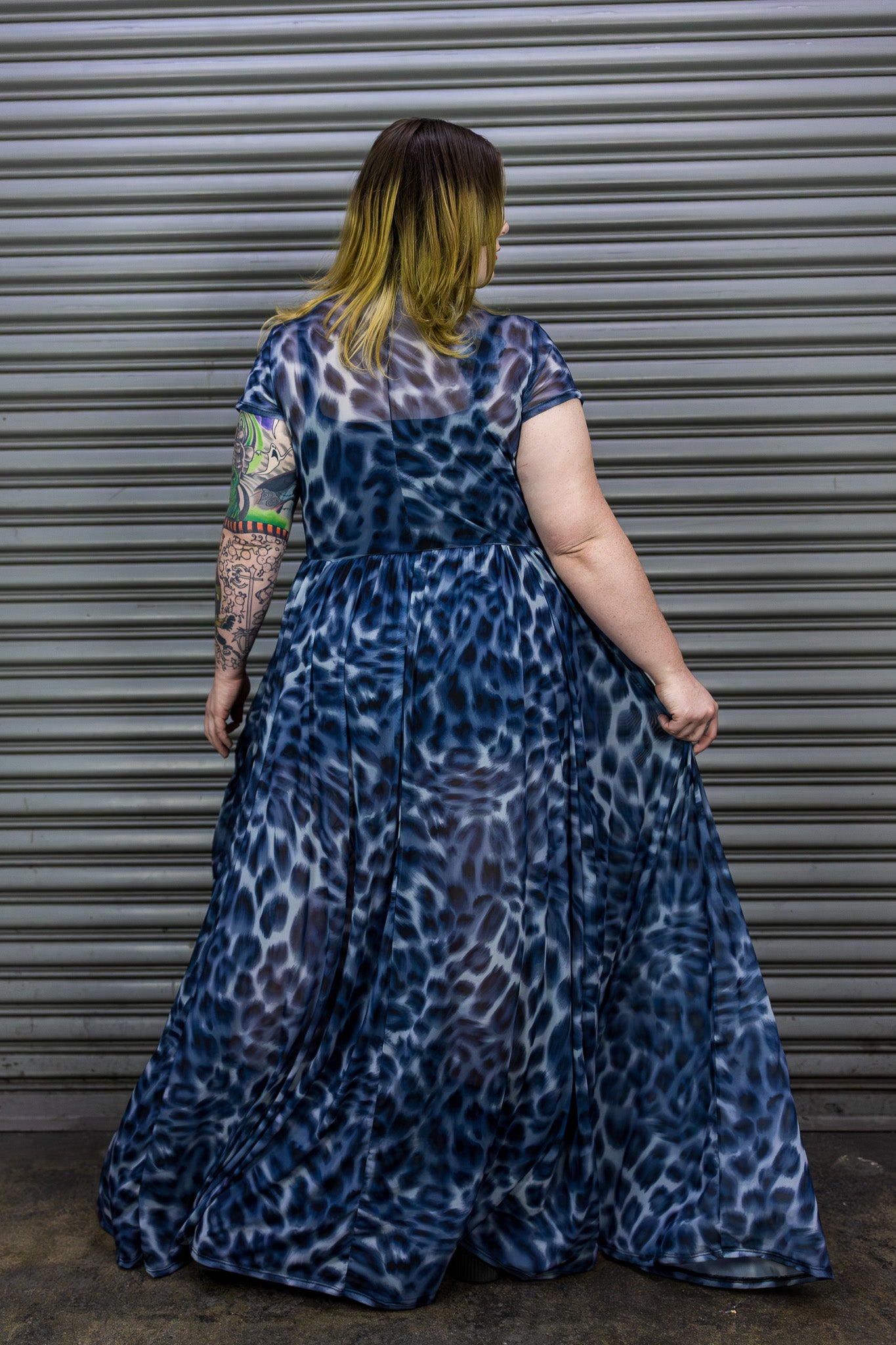 Person wearing a blue leopard print maxi dress standing in front of a metal shutter.