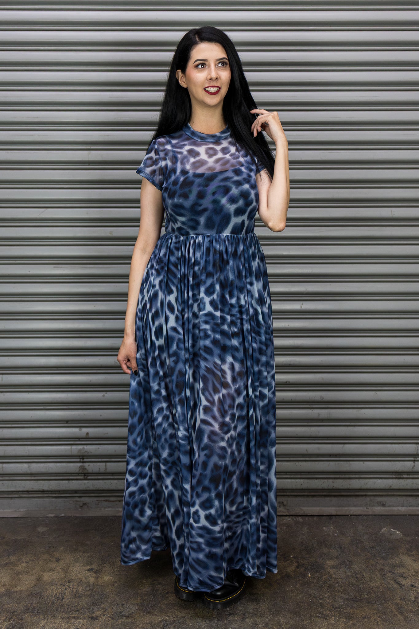 Woman wearing a blue patterned maxi dress standing in front of a metal shutter.