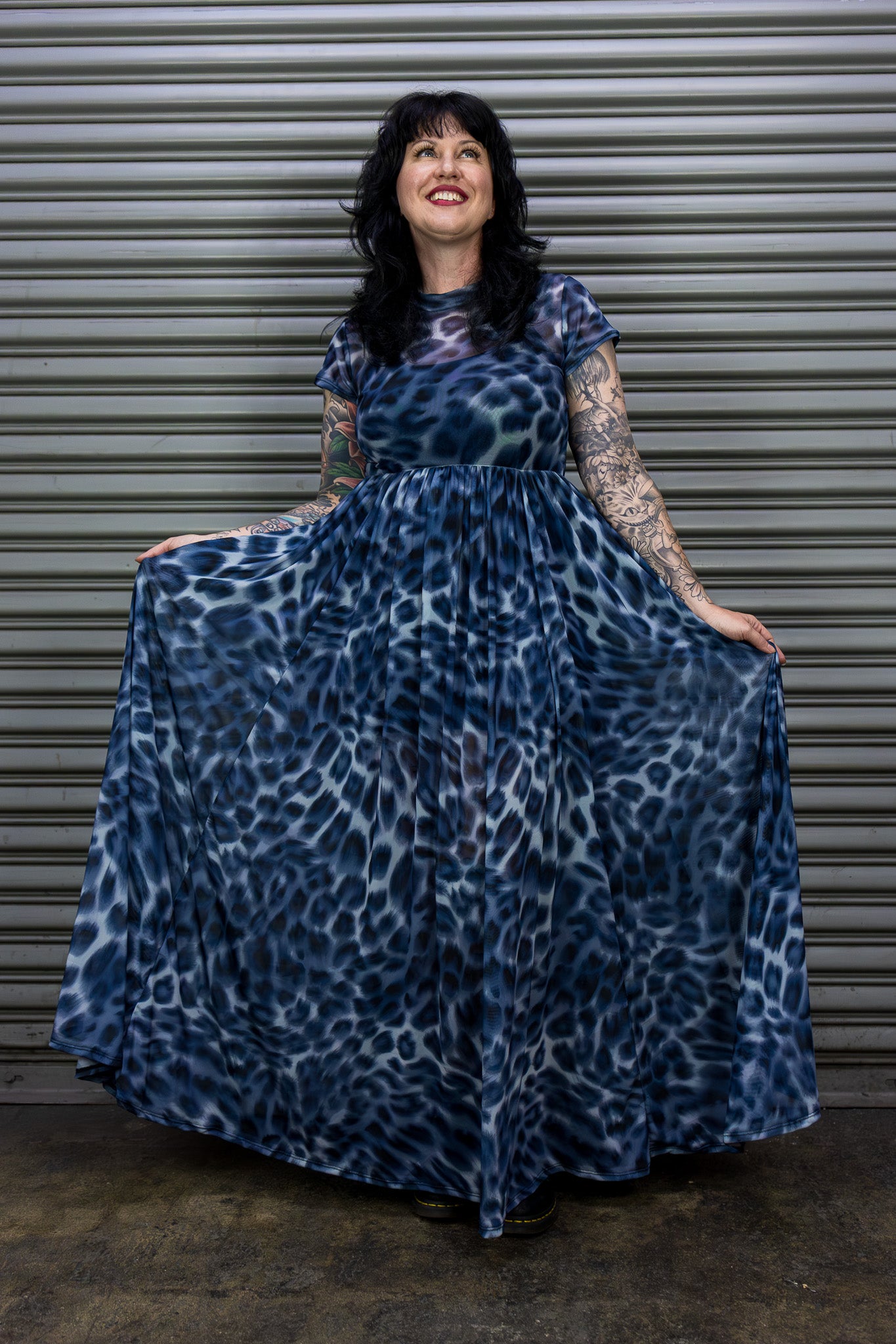 Woman wearing a blue leopard print dress standing against a metal shutter.