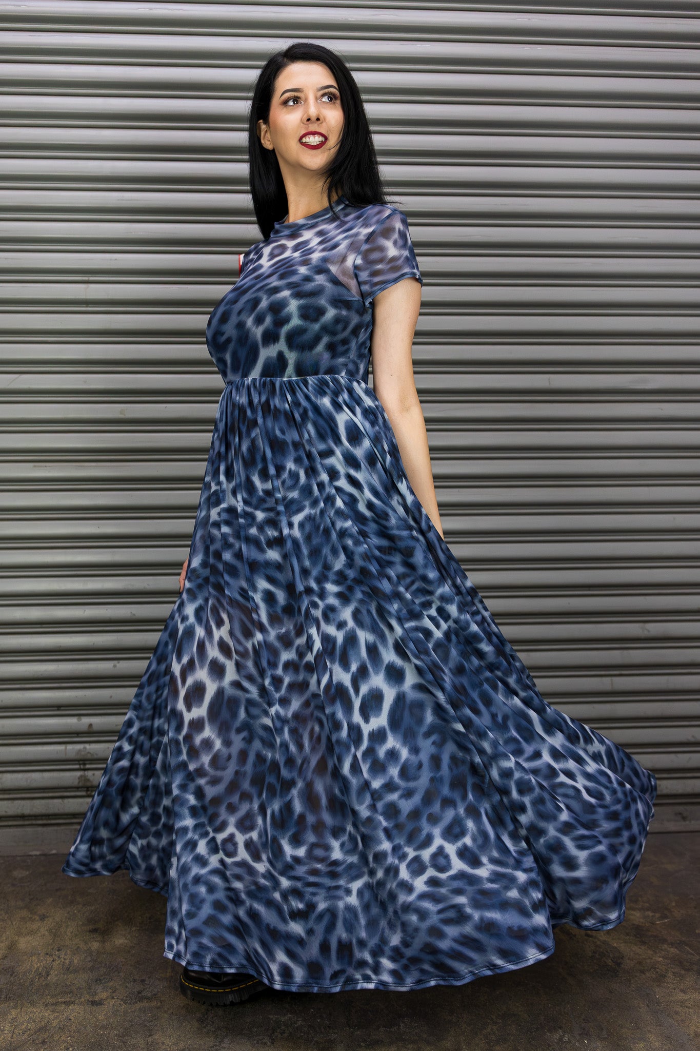 Woman wearing a blue leopard print dress in front of a corrugated metal wall.