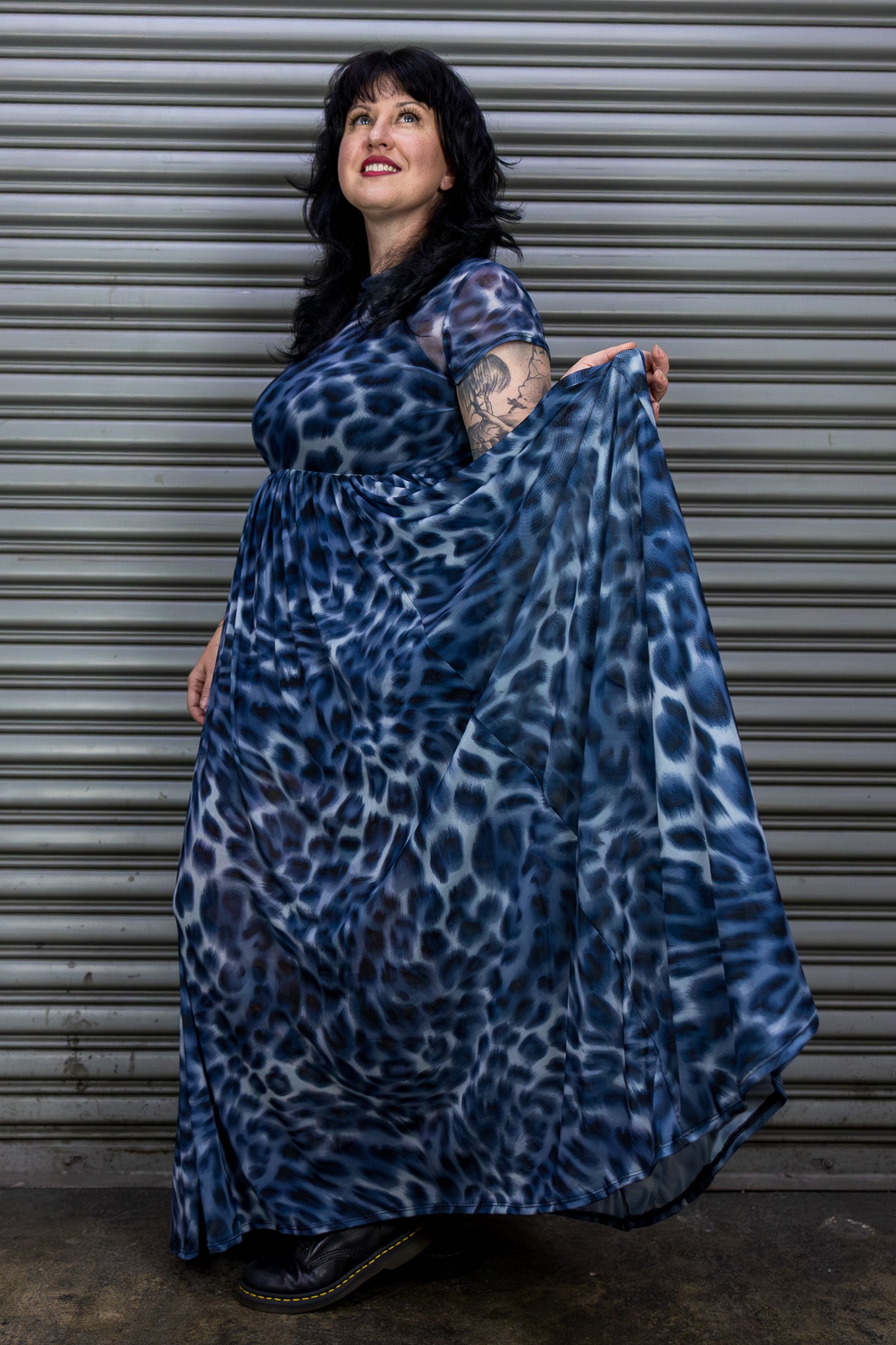 Woman holding a blue leopard print dress against a metal shutter background.