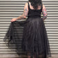 Person wearing a black dress with sheer overlay in front of a metallic shutter.